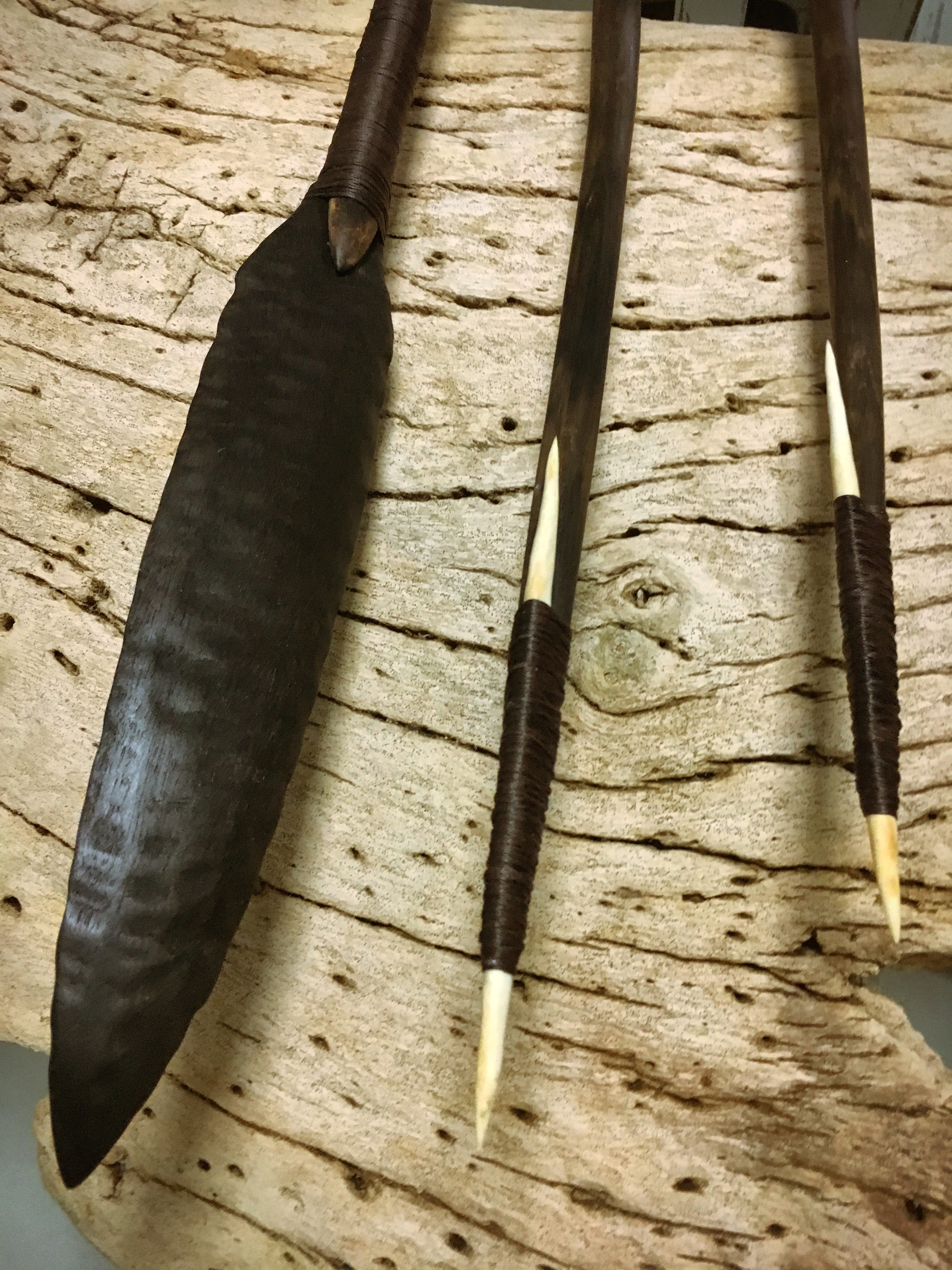 the tips of three spears rest on a smoothed out wooden plank, the left most spear is tipped with a flat broad head the two right most spears are tipped with a thin fine bone head.